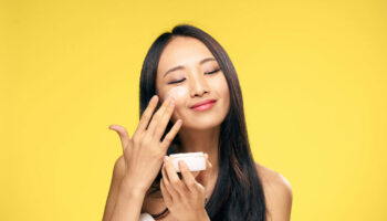 1045364 Woman puts cream on face on yellow background